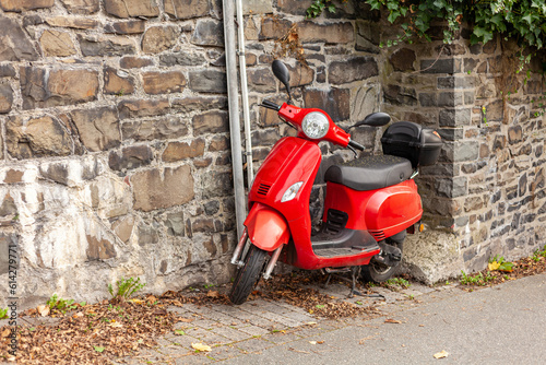 Red scooter parked on the street in front of a stone wall