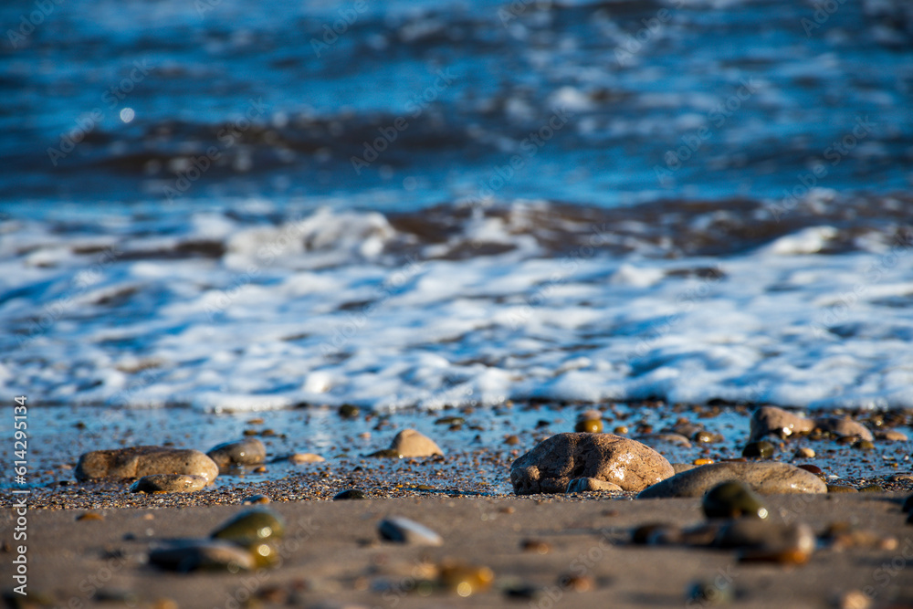 Selective focus on the sand and stones of a beach with the sea breaker in the background. Selective focus on the sand and stones of a beach with the sea breaker in the background.