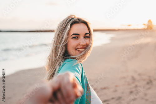 Portrait close up of one young beautiful attractive blonde woman walking on the beach holding boyfriend’s hand looking at the camera. Enjoying free time at vacations concept lifestyle. © Daniel