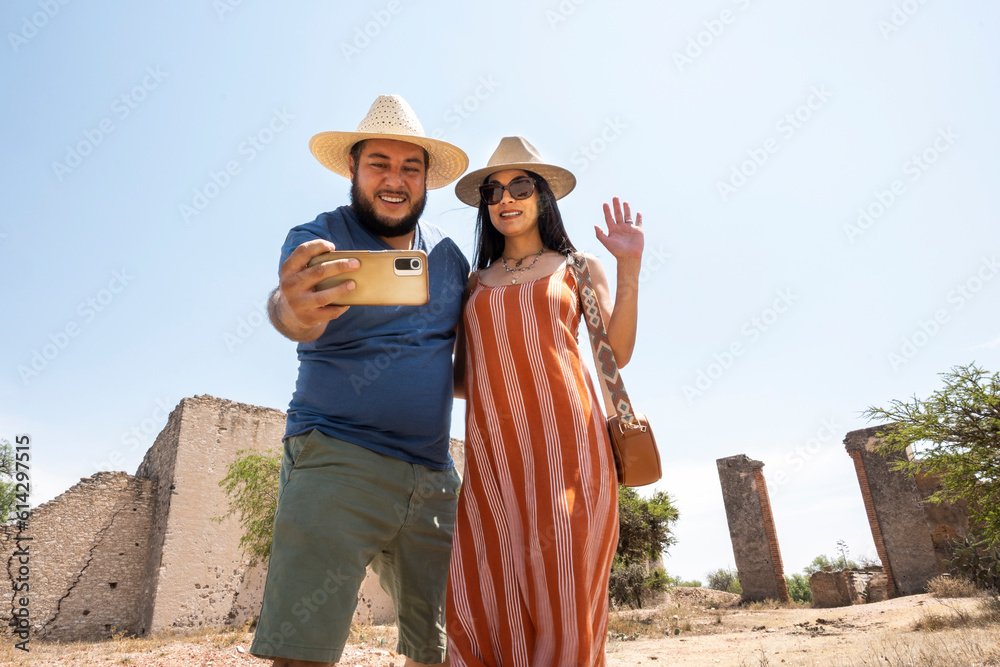 married couple take selfies on their trip on a sunny afternoon with some ruins behind