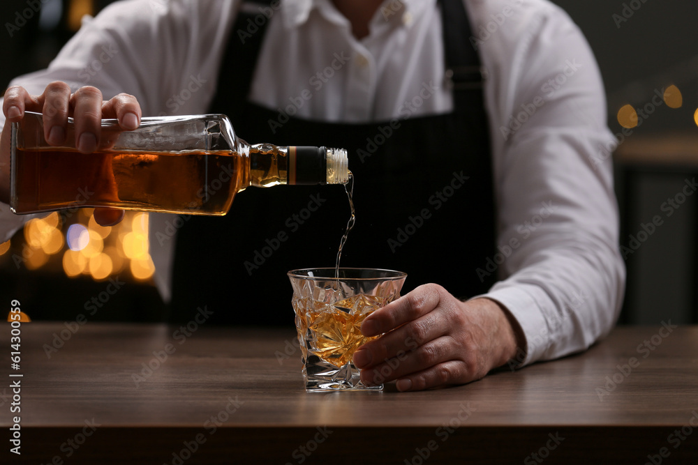 Bartender pouring whiskey from bottle into glass at bar counter indoors, closeup