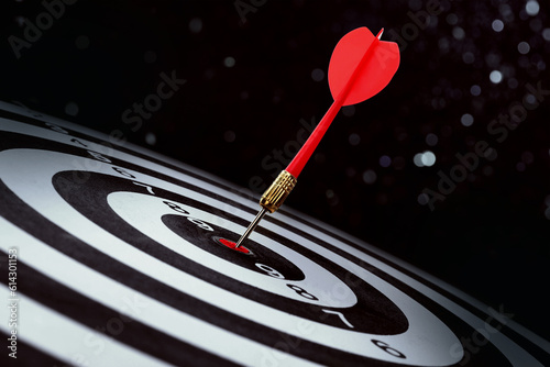 Dart board with red arrow hitting target against black background, bokeh effect