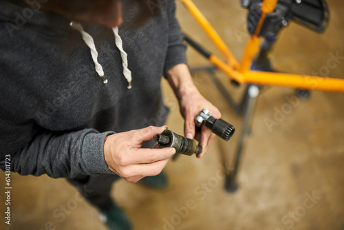 Bicycle mechanic looks at a hub axle he has just removed from a bike at his repair shop. Top view composition with copy space.