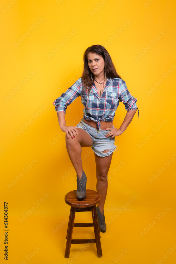 Portrait of beautiful woman with her foot on top of a wooden stool. Dressed in a June character with a checkered blouse. Sao Joao party. Portrait of beautiful woman with her foot on top of a wooden stool. Dressed in a June character with a checkered blouse. Sao Joao party.