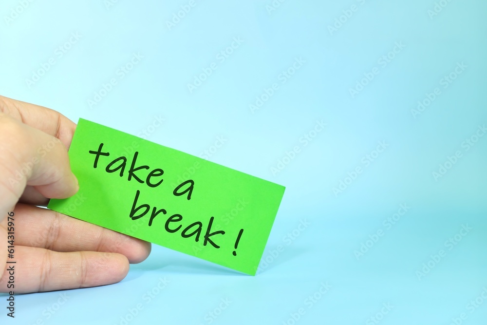 Take a break reminder concept. Hand holding a bright green paper message note. Take a break reminder concept. Hand holding a bright green paper message note.