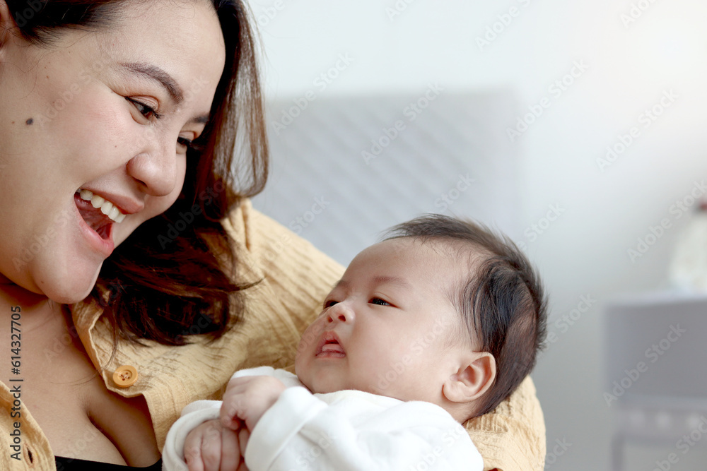 Mother holds infant newborn baby boy in arm and plays with him on bed in bedroom, lovely family mom and child stand time together, parent take care kid, overweight mom with fat body after childbirth.