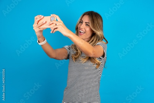young beautiful woman wearing striped t-shirt taking a selfie to post it on social media or having a video call with friends.