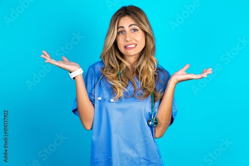 Fotografie Clueless Young caucasian blonde doctor woman wearing blue uniform shrugs shoulde