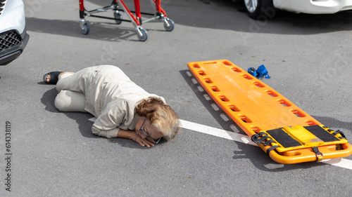 An elderly woman lays down on the road after a traffic accident next with a stretcher.