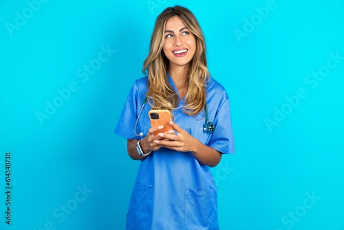 Young caucasian blonde doctor woman wearing blue uniform hold telephone hands read good youth news look empty space advert