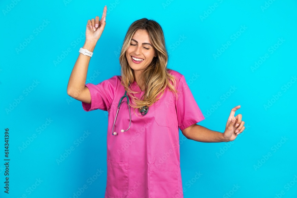 Photo of upbeat Young caucasian blonde doctor woman wearing pink uniform has fun and dances carefree wear being in perfect mood makes movements. Spends free time on disco party