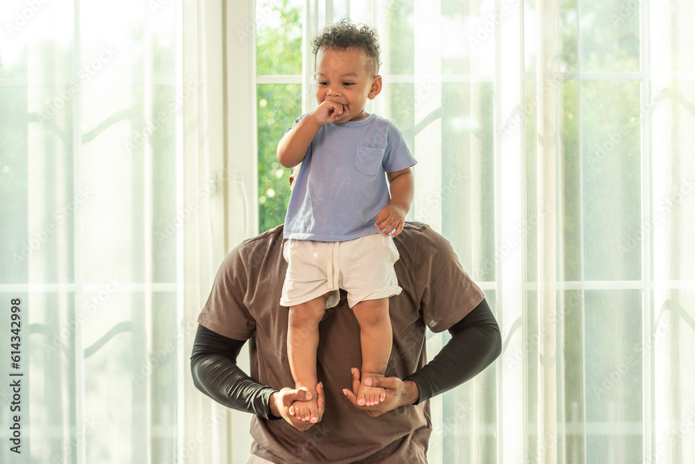 Happy african black parents dad father throw baby son on piggyback and neck riding teasing fun near window. Black baby son and daddy enjoy teasing kiss cheek and neck riding at window light Happy african black parents dad father throw baby son on piggyback and neck riding teasing fun near window. Black baby son and daddy enjoy teasing kiss cheek and neck riding at window light