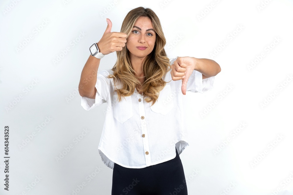 Young caucasian business woman wearing white shirt over white background showing thumbs up and thumbs down, difficult choose concept Young caucasian business woman wearing white shirt over white background showing thumbs up and thumbs down, difficult choose concept