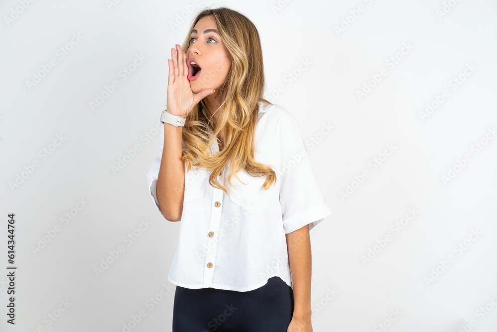 Young caucasian business woman wearing white shirt over white background shouting and screaming loud to side with hand on mouth. Communication concept. Young caucasian business woman wearing white shirt over white background shouting and screaming loud to side with hand on mouth. Communication concept.