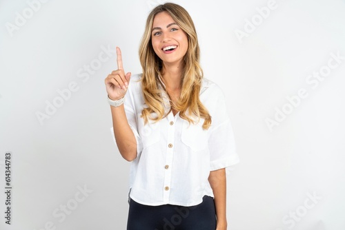 Young caucasian business woman wearing white shirt over white background pointing finger up and looking inspired by genius thought, showing good idea sign, having clever solution in mind