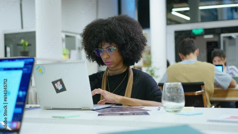 Young black businesswoman sitting at workplace in open space office and working on laptop. Medium handheld shot Young black businesswoman sitting at workplace in open space office and working on laptop. Medium handheld shot