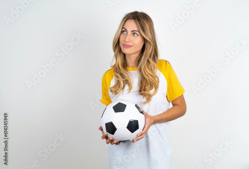 Charming thoughtful Young beautiful woman wearing football T-shirt over white background stands with arms folded concentrated somewhere with pensive expression thinks what to do © Jihan