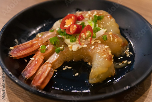 Pickled Botan Ebi shrimp with soy sauce on black dish.
