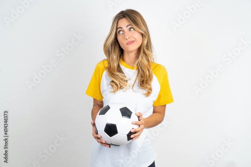 Dissatisfied Young beautiful woman wearing football T-shirt over white background purses lips and has unhappy expression looks away stands offended. Depressed frustrated model. © Jihan