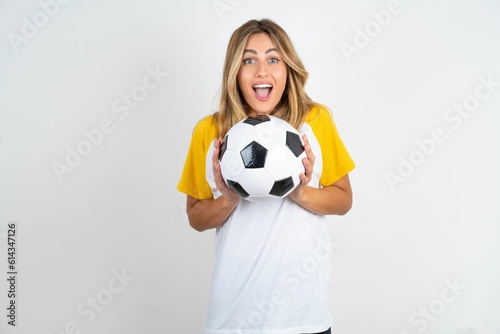 Delighted positive Young beautiful woman wearing football T-shirt over white background opens mouth  and arms palms up after having great result