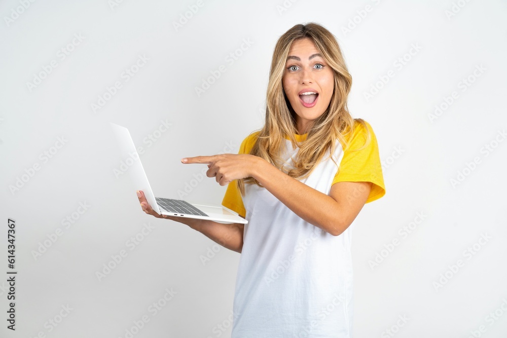 Shocked Young beautiful woman wearing football T-shirt over white background pointing finger modern device Shocked Young beautiful woman wearing football T-shirt over white background pointing finger modern device