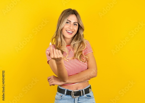 Foto Young beautiful blonde woman wearing striped t-shirt over yellow studio backgrou