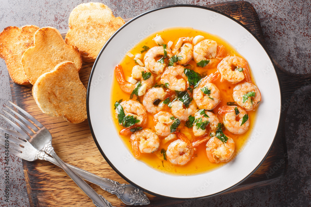 Gambas al ajillo or garlic shrimp is a traditional Spanish tapas made by combining fresh shrimp with an ajillo sauce on the wooden board. Horizontal top view from above