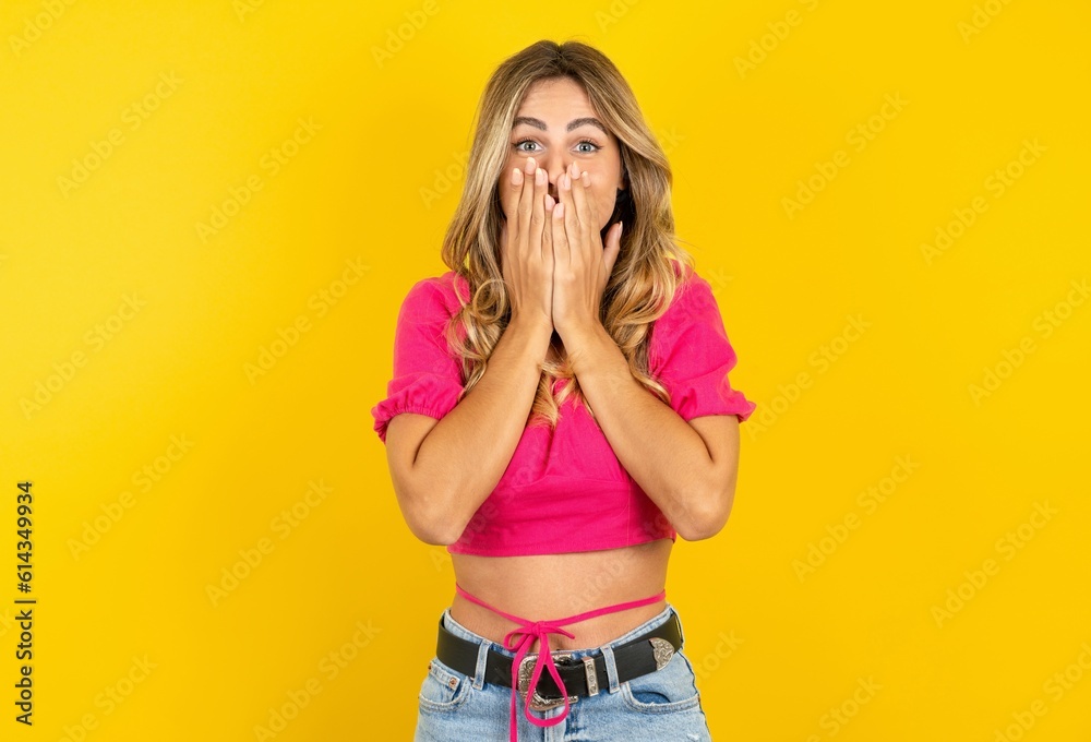 Vivacious young blonde woman wearing pink crop top over yellow studio background, giggles joyfully, covers mouth, has natural laughter, hears positive story or funny anecdote Vivacious young blonde woman wearing pink crop top over yellow studio background, giggles joyfully, covers mouth, has natural laughter, hears positive story or funny anecdote