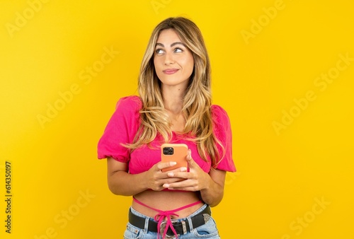 young blonde woman wearing pink crop top over yellow studio background holds telephone hands reads good youth news look empty space advert