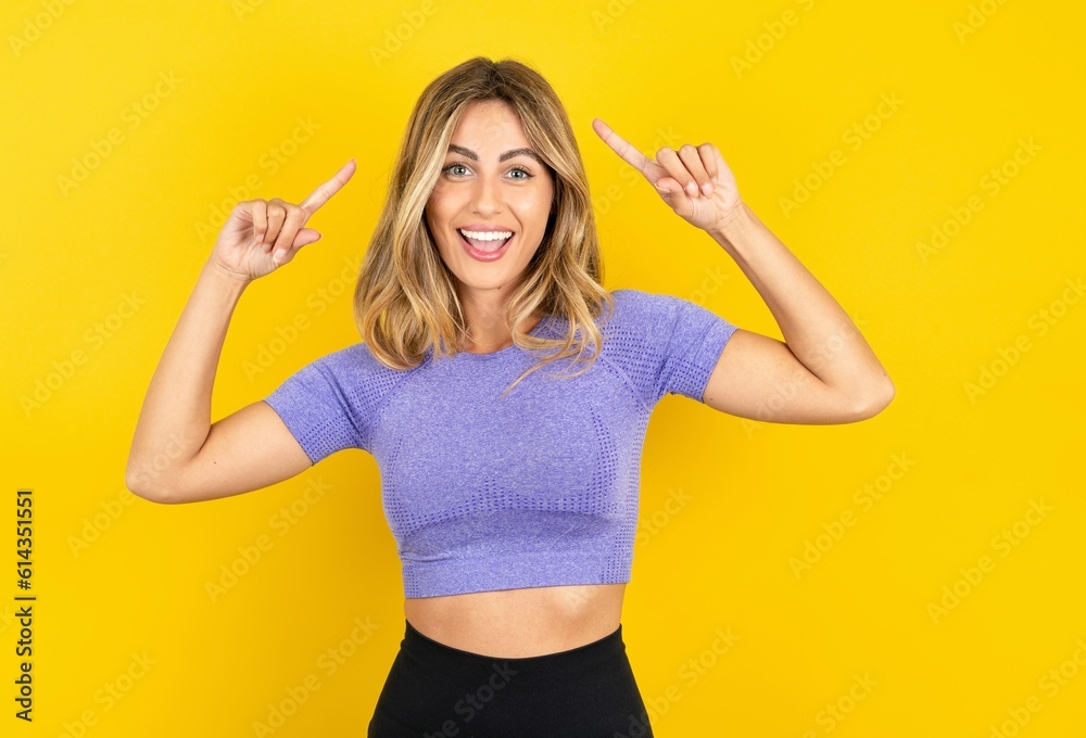 Fototapeta premium Cheerful Young beautiful blonde woman wearing sportswear over yellow studio background demonstrating hairdo