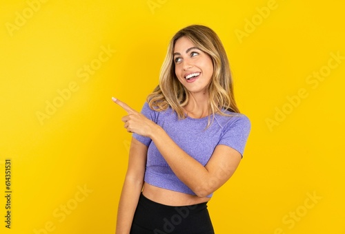 Young beautiful blonde woman wearing sportswear over yellow studio background glad cheery demonstrating copy space look novelty