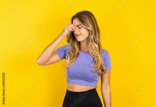 Sad Young beautiful blonde woman wearing sportswear over yellow studio background suffering from headache holding hand on her face