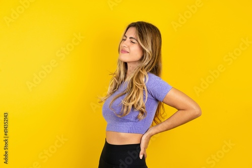 Young beautiful blonde woman wearing sportswear over yellow studio background got back pain