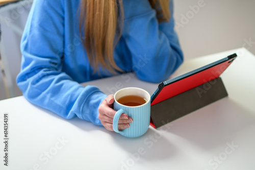 Kobieta pijąca herbatę, siedząca przy stole przed ekranem tableta