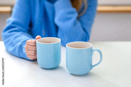 Dziewczyna siedząca przy stole z dwoma kubkami herbaty czeka...