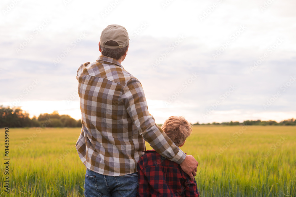 Farmer and his son in front of a sunset agricultural landscape. Man and a boy in a countryside field. Fatherhood, country life, farming and country lifestyle concept. Farmer and his son in front of a sunset agricultural landscape. Man and a boy in a countryside field. Fatherhood, country life, farming and country lifestyle concept.