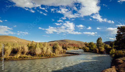 Wide river on a background of rocky mountains under blue sky with white clouds. Picturesque sunny summer landscape of Kurai steppe, Altai, Siberia, Russia.