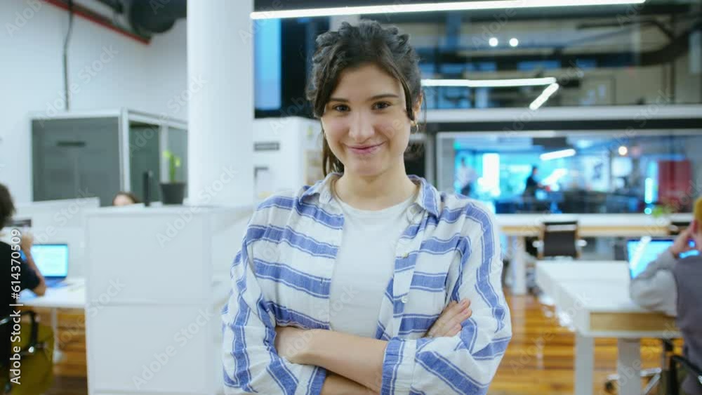 Young pretty businesswoman smiling and posing on camera with arms crossed in modern open space office during the day. Video portrait, medium shot Young pretty businesswoman smiling and posing on camera with arms crossed in modern open space office during the day. Video portrait, medium shot
