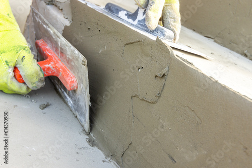 Detail of a man's hand in work gloves and a trowel with a lump of cement-based tile adhesive. Leveling the adhesive layer as a preparation before gluing the tile.