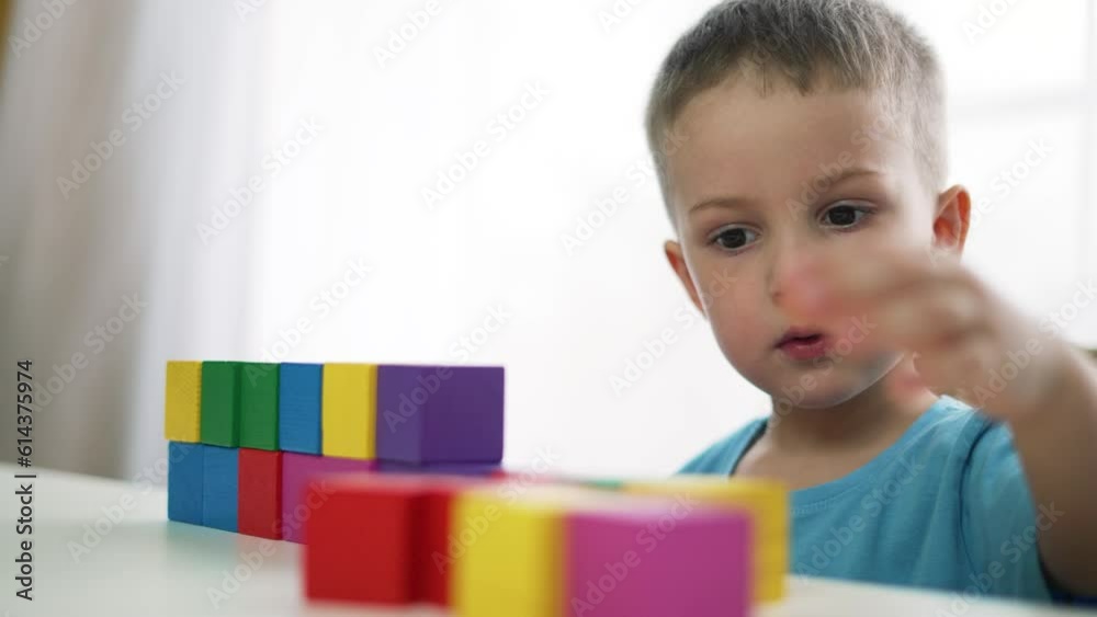 Adorable children play in kindergarten and at home. Colored cubes and toys on table. Child collects toys in kindergarten. Child home game. Concept of family happy.Kid with colored cubes plays at table Adorable children play in kindergarten and at home. Colored cubes and toys on table. Child collects toys in kindergarten. Child home game. Concept of family happy.Kid with colored cubes plays at table