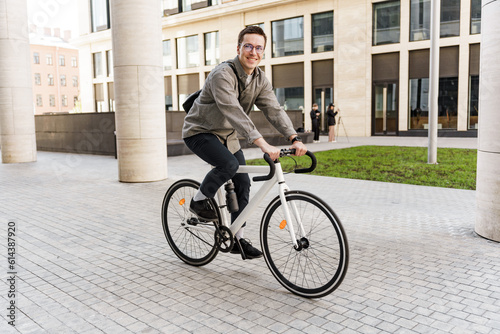 A happy entrepreneur guy with a business bag uses environmentally friendly transport. A man in formal attire is smiling on a bicycle and has arrived at work career in the office.