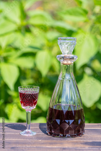 Cuadro en lienzo Homemade cherry brandy in glasses and in a bottle on a wooden table in a summer