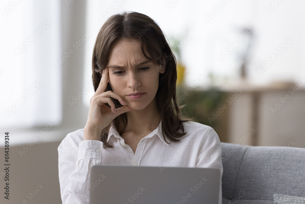 Frowning woman sit on sofa looks at laptop screen having dilemma or difficult on-line task, read unpleasant news, feeling negative emotions, learn new program or app, lack of understanding or ideas Frowning woman sit on sofa looks at laptop screen having dilemma or difficult on-line task, read unpleasant news, feeling negative emotions, learn new program or app, lack of understanding or ideas