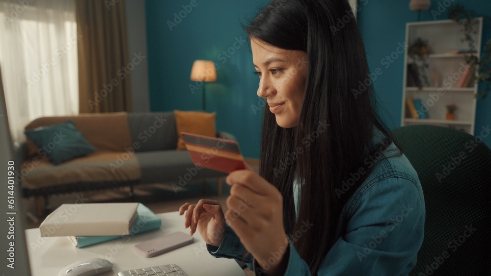 A young attractive girl uses a computer and a credit card to pay for online purchases close up. Asian woman smiling contentedly after making a successful purchase. A young attractive girl uses a computer and a credit card to pay for online purchases close up. Asian woman smiling contentedly after making a successful purchase.
