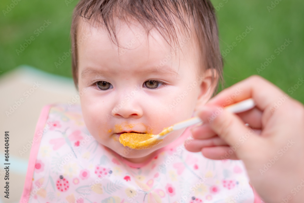 woman feeding her beautiful little daughter - mother hand and close up portrait of adorable and happy baby girl eating baby porridge from spoon in health and nutrition concept woman feeding her beautiful little daughter - mother hand and close up portrait of adorable and happy baby girl eating baby porridge from spoon in health and nutrition concept