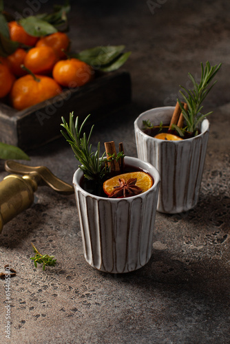 Mulled wine in ceramic glasses with tangerines,fresh rosemary,thyme,cinnamon and anise stars.Winter or Christmas hot drink.