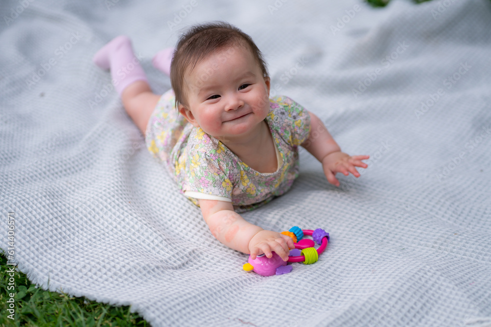 Fototapeta premium adorable and happy baby girl hat embraces the joys of playfulness on a soft blanket playing with little toy. Laughing as she explores the natural wonders of an outdoors city park