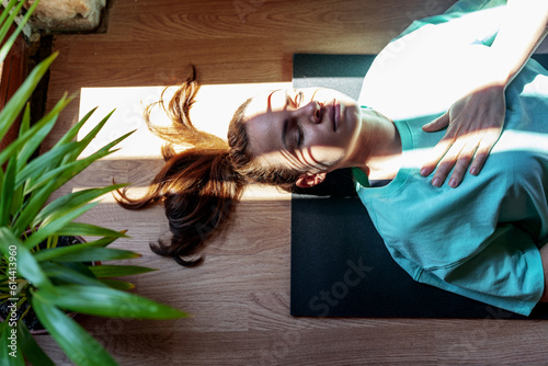 Yoga breathing exercise, serene woman lying down on exercise mat on back with closed eyes and meditating. photo