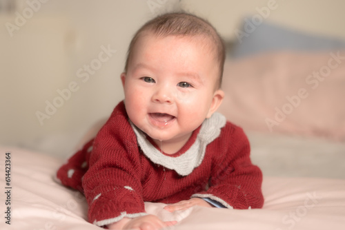 adorable and happy 5 months old baby girl gleefully discovers boundless joy while playfully exploring her bed. Surrounded by the warm glow of natural light the little on smiles cheerfully