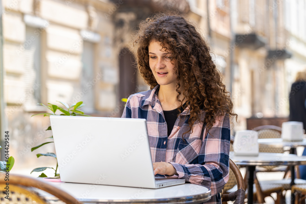 Young woman working online distant job with laptop in city sunshine street cafe or restaurant browsing website chatting outdoors during break. Girl tourist looking computer screen. Town lifestyles Young woman working online distant job with laptop in city sunshine street cafe or restaurant browsing website chatting outdoors during break. Girl tourist looking computer screen. Town lifestyles